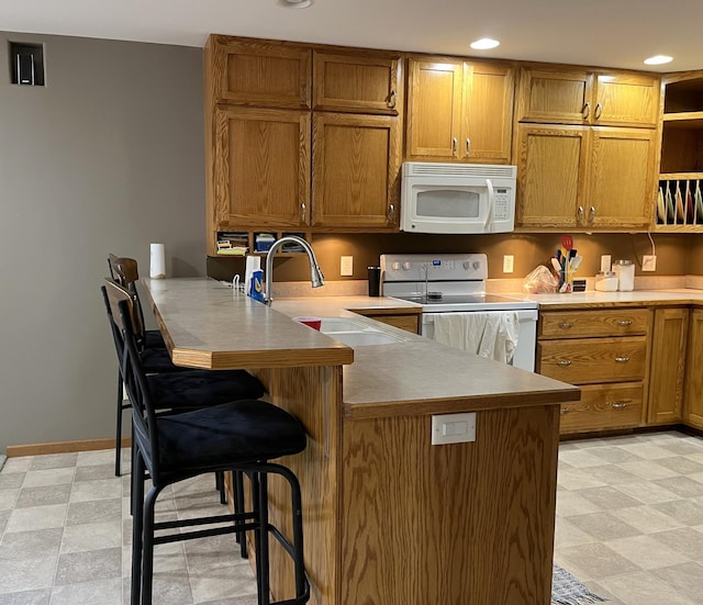 kitchen with white appliances, a breakfast bar area, sink, and kitchen peninsula