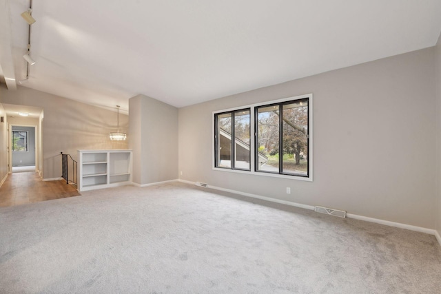 unfurnished living room with a chandelier, track lighting, and carpet floors