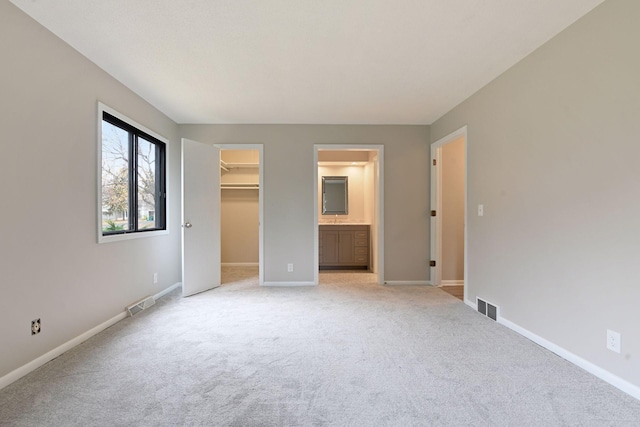 unfurnished bedroom with connected bathroom, a closet, a spacious closet, and light carpet