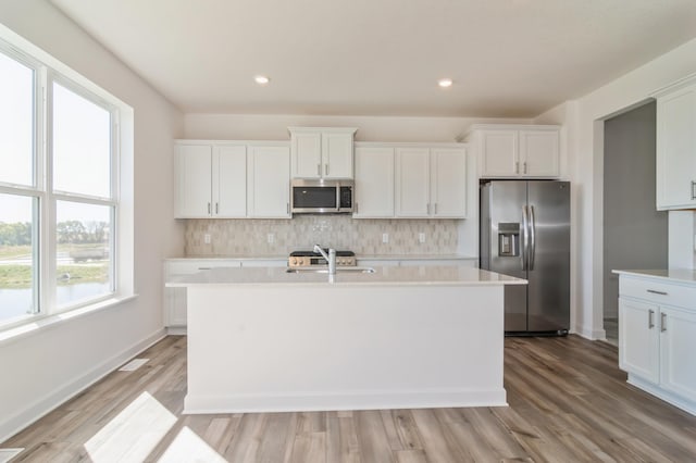 kitchen with white cabinetry, stainless steel appliances, a center island with sink, and light hardwood / wood-style flooring