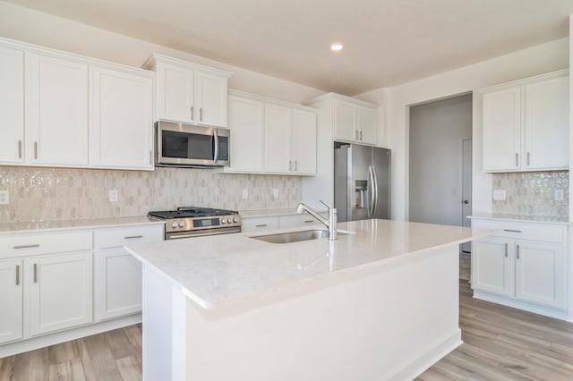 kitchen with light wood-type flooring, white cabinets, a center island with sink, and stainless steel appliances