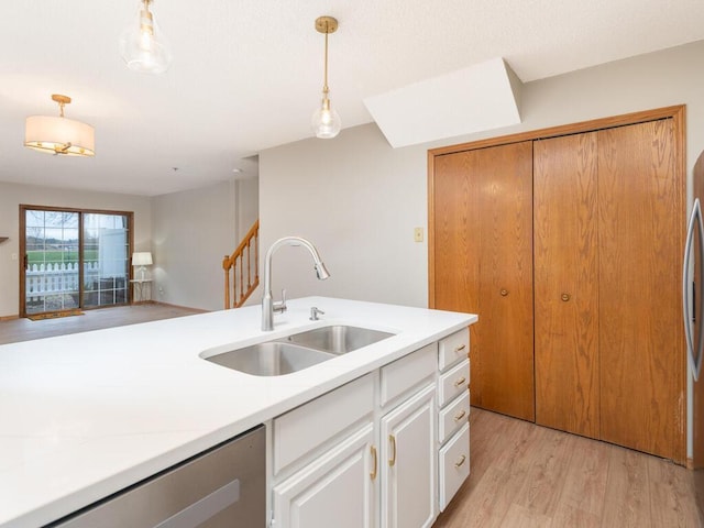 kitchen with sink, white cabinets, light wood-type flooring, stainless steel dishwasher, and pendant lighting