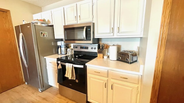 kitchen featuring stainless steel appliances, light wood-type flooring, a textured ceiling, and white cabinetry