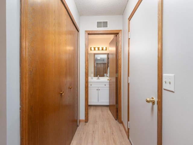 hall featuring sink, a textured ceiling, and light hardwood / wood-style flooring