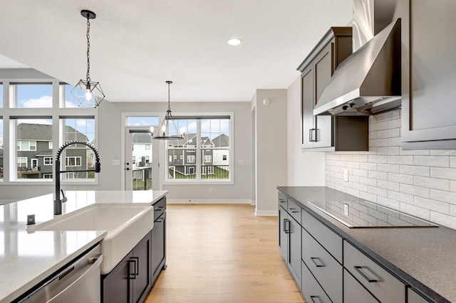 kitchen featuring black electric stovetop, a notable chandelier, decorative light fixtures, stainless steel dishwasher, and wall chimney exhaust hood