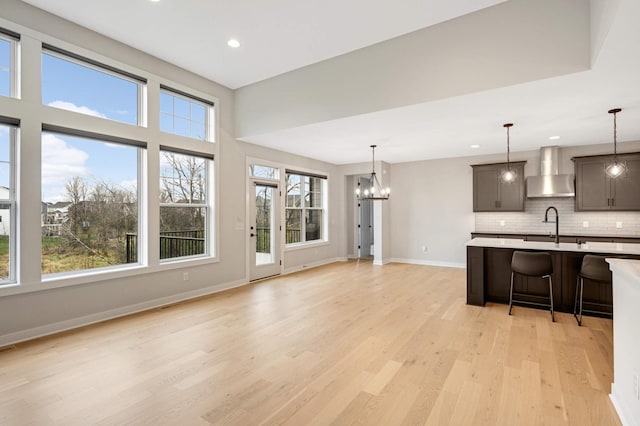 kitchen with pendant lighting, a breakfast bar area, a notable chandelier, light hardwood / wood-style floors, and wall chimney exhaust hood