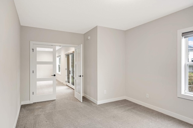 spare room featuring light carpet, french doors, and a healthy amount of sunlight