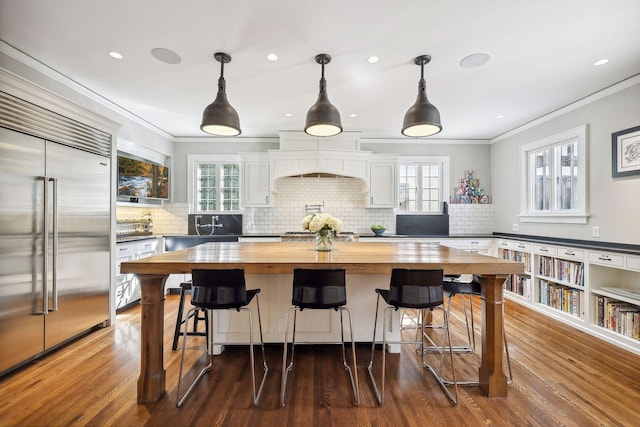 kitchen with decorative light fixtures, white cabinetry, stainless steel built in fridge, and butcher block counters