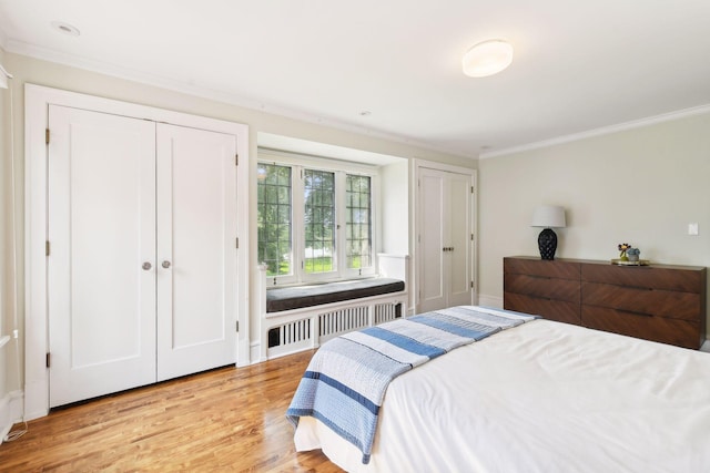 bedroom with light hardwood / wood-style floors, radiator heating unit, crown molding, and two closets