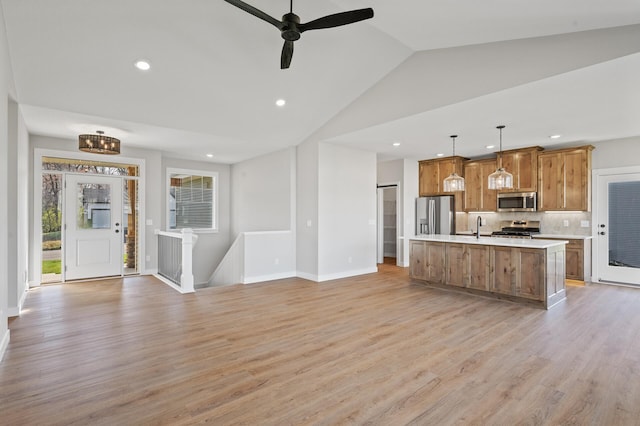 kitchen featuring pendant lighting, light hardwood / wood-style flooring, vaulted ceiling, an island with sink, and stainless steel appliances