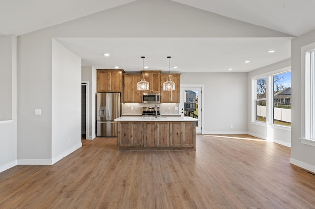 kitchen with light wood-type flooring, stainless steel appliances, pendant lighting, a center island with sink, and lofted ceiling