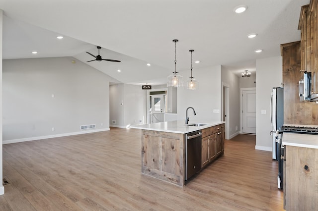 kitchen featuring hanging light fixtures, light hardwood / wood-style floors, vaulted ceiling, a center island with sink, and appliances with stainless steel finishes