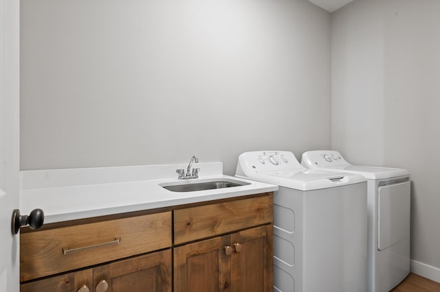 clothes washing area featuring separate washer and dryer, sink, and cabinets