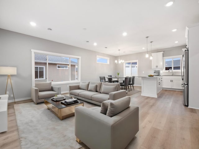 living room with plenty of natural light, a notable chandelier, sink, and light hardwood / wood-style flooring