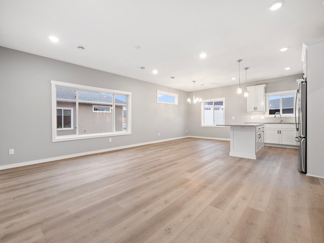 interior space with stainless steel fridge, a kitchen island, light wood-type flooring, pendant lighting, and white cabinets