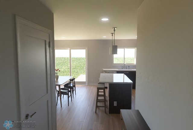 kitchen with sink, hanging light fixtures, a kitchen breakfast bar, a kitchen island, and light wood-type flooring