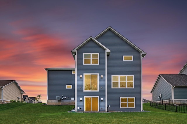 back house at dusk featuring a lawn