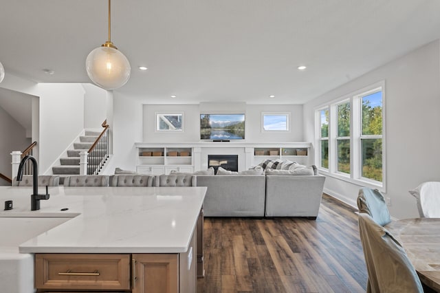 kitchen featuring hanging light fixtures, dark wood-type flooring, light stone countertops, and sink