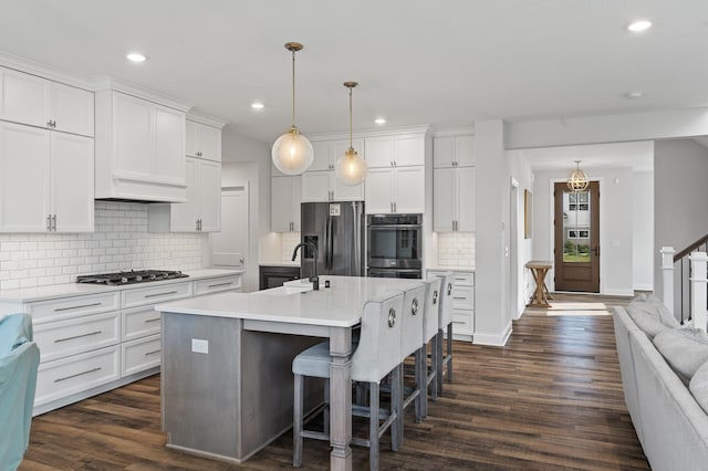 kitchen with stainless steel appliances, white cabinetry, a kitchen island with sink, and decorative light fixtures