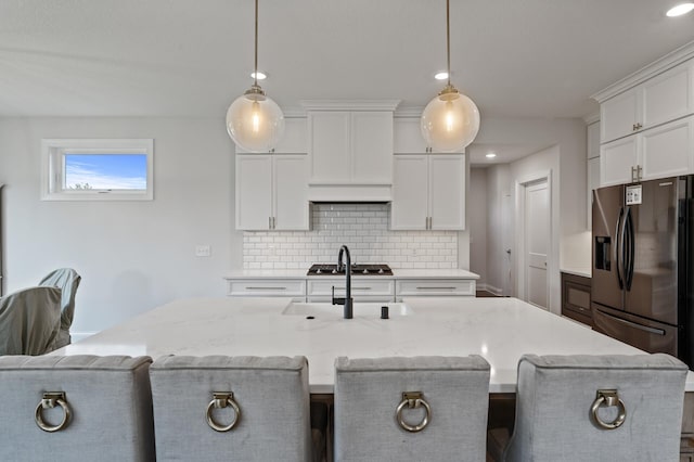 kitchen featuring light stone countertops, a kitchen island with sink, pendant lighting, and white cabinets