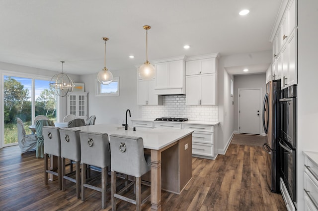 kitchen with hanging light fixtures, white cabinetry, and an island with sink