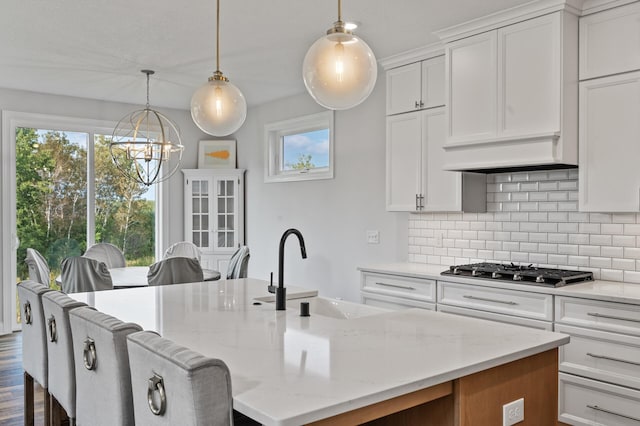 kitchen featuring pendant lighting, white cabinetry, sink, stainless steel gas cooktop, and a kitchen island with sink