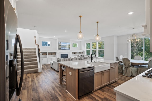 kitchen featuring sink, decorative light fixtures, dark hardwood / wood-style flooring, black dishwasher, and a kitchen island with sink