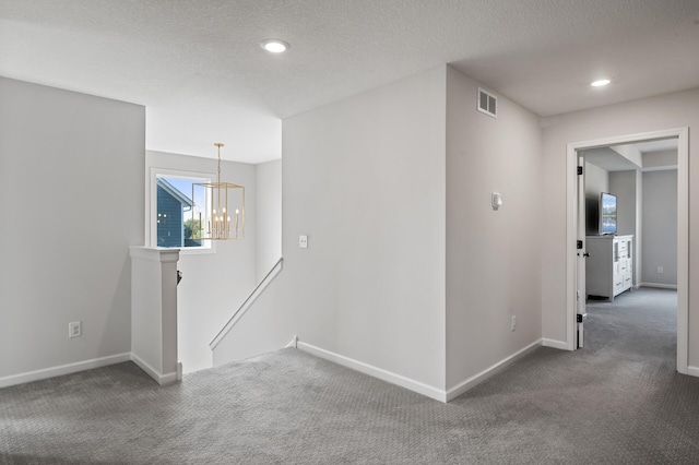 corridor featuring an inviting chandelier, a textured ceiling, and dark carpet