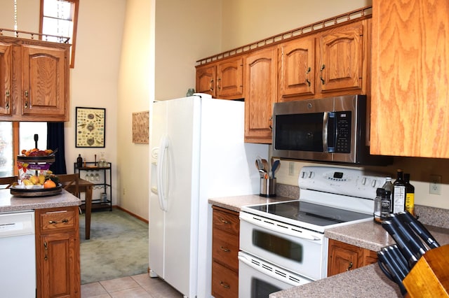 2935 Acorn Ln NE, Bemidji, MN 56601 - kitchen featuring white appliances, light carpet, brown cabinetry, light tile patterned flooring, and a towering ceiling
