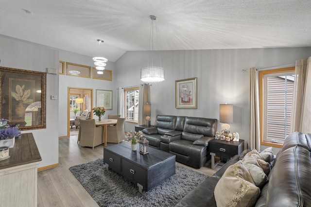 living room with a textured ceiling, a chandelier, light hardwood / wood-style floors, and vaulted ceiling