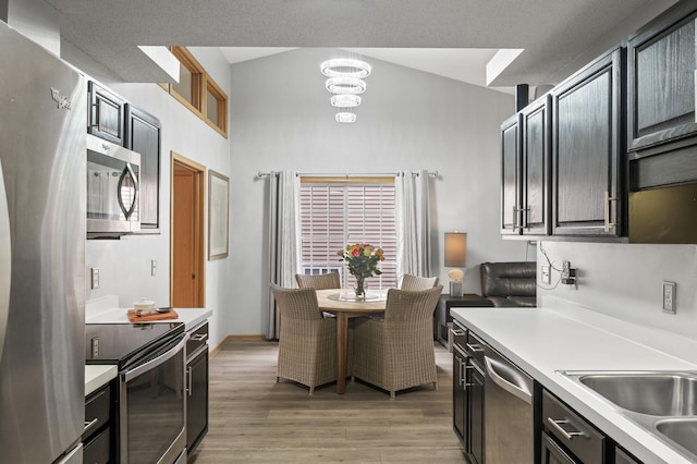 kitchen featuring lofted ceiling, sink, light wood-type flooring, a notable chandelier, and stainless steel appliances