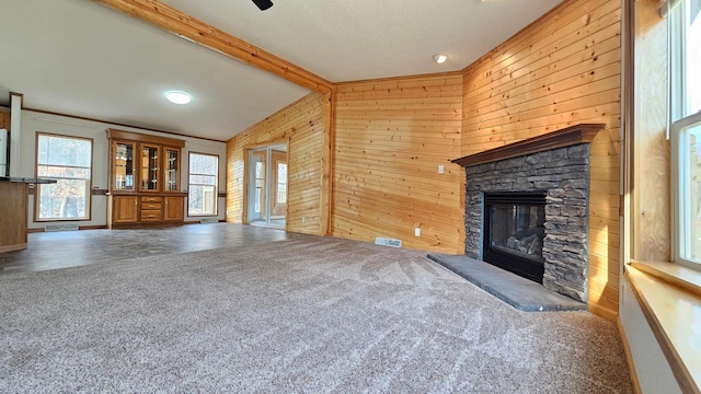 unfurnished living room featuring wooden walls, a fireplace, lofted ceiling with beams, and dark colored carpet