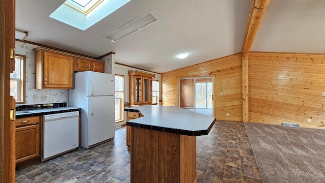 kitchen with wood walls, lofted ceiling with skylight, a textured ceiling, white appliances, and a kitchen island