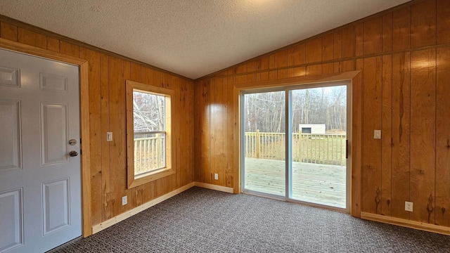 entryway featuring lofted ceiling, a textured ceiling, carpet floors, and wooden walls