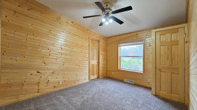 unfurnished bedroom featuring carpet, ceiling fan, a textured ceiling, and wooden walls