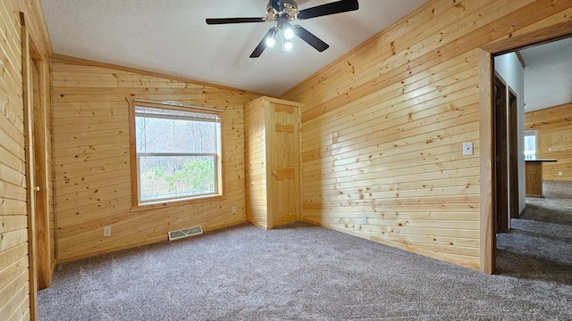 carpeted spare room featuring ceiling fan, lofted ceiling, and wooden walls