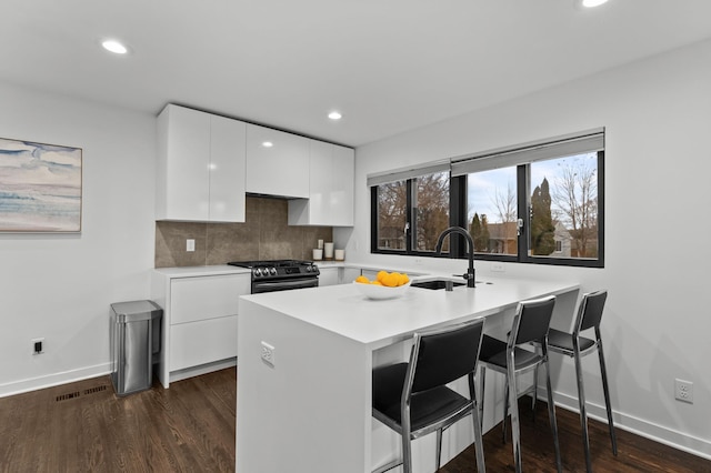 kitchen with white cabinetry, dark wood-type flooring, kitchen peninsula, black gas stove, and a breakfast bar