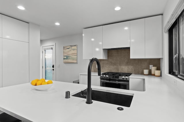 kitchen featuring backsplash, kitchen peninsula, stainless steel gas range oven, and white cabinets