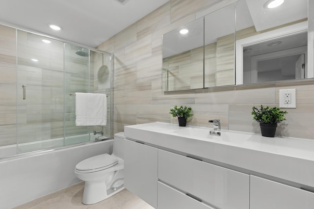 full bathroom with shower / bath combination with glass door, vanity, tile walls, and toilet