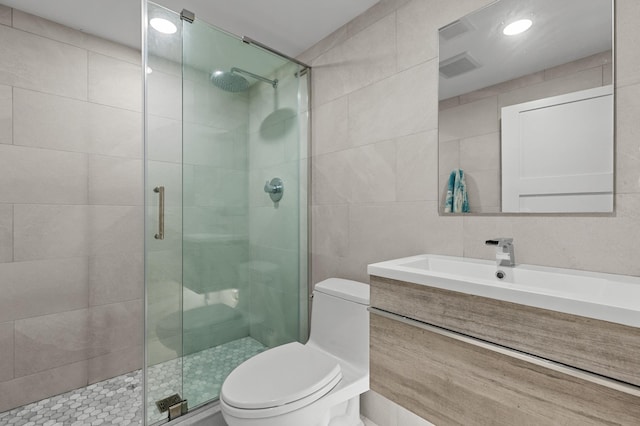 bathroom featuring vanity, toilet, a shower with door, and tile walls