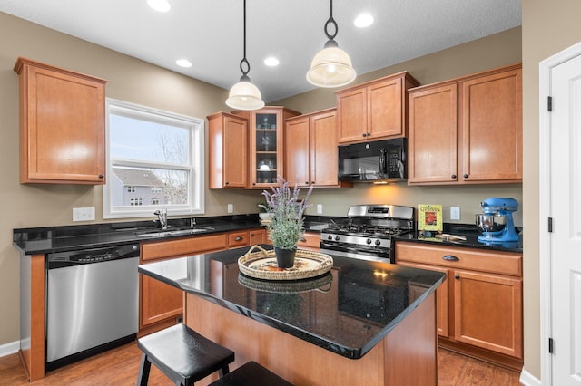 kitchen with a sink, light wood-style floors, appliances with stainless steel finishes, a kitchen bar, and decorative light fixtures