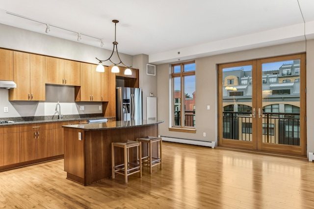 kitchen with a center island, baseboard heating, dark stone countertops, stainless steel fridge, and light hardwood / wood-style floors