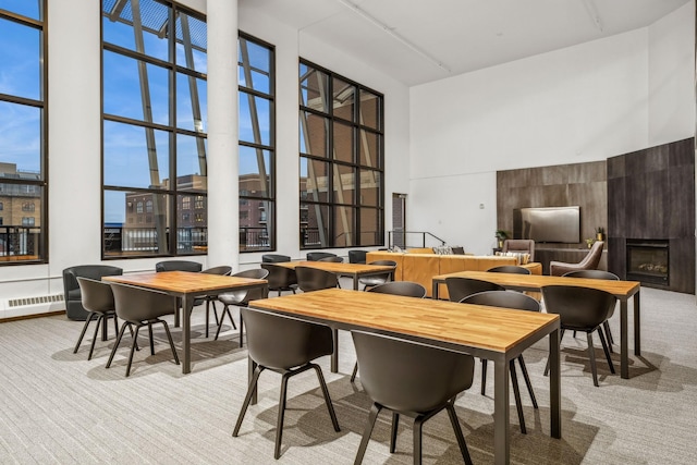 dining area with a towering ceiling, a large fireplace, and carpet