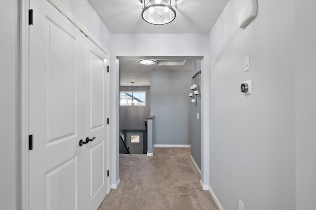 corridor with a textured ceiling, light carpet, and a notable chandelier