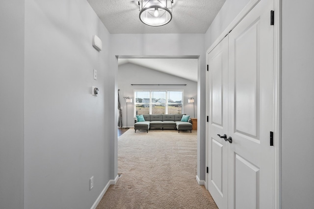 corridor with lofted ceiling, a textured ceiling, and light carpet