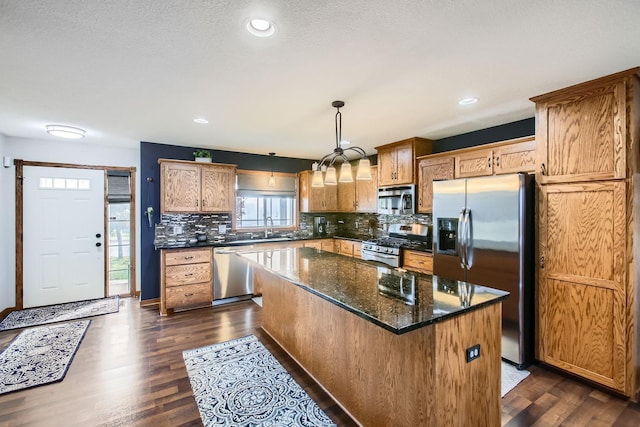 kitchen featuring dark wood-type flooring, hanging light fixtures, dark stone countertops, a kitchen island, and appliances with stainless steel finishes