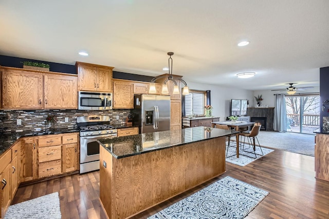 kitchen with appliances with stainless steel finishes, dark wood-type flooring, decorative light fixtures, a fireplace, and a center island