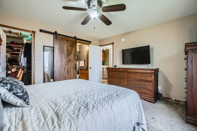 bedroom with light carpet, ceiling fan, a barn door, a spacious closet, and a textured ceiling