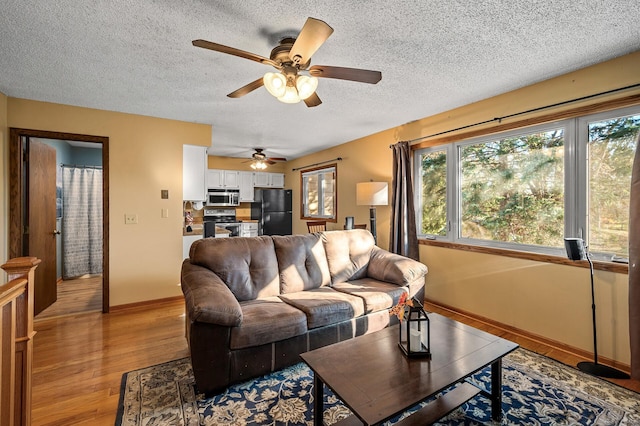 living room featuring light wood-type flooring, a textured ceiling, and ceiling fan