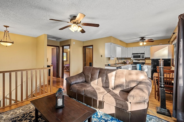 living room featuring a textured ceiling, sink, ceiling fan, and light hardwood / wood-style flooring